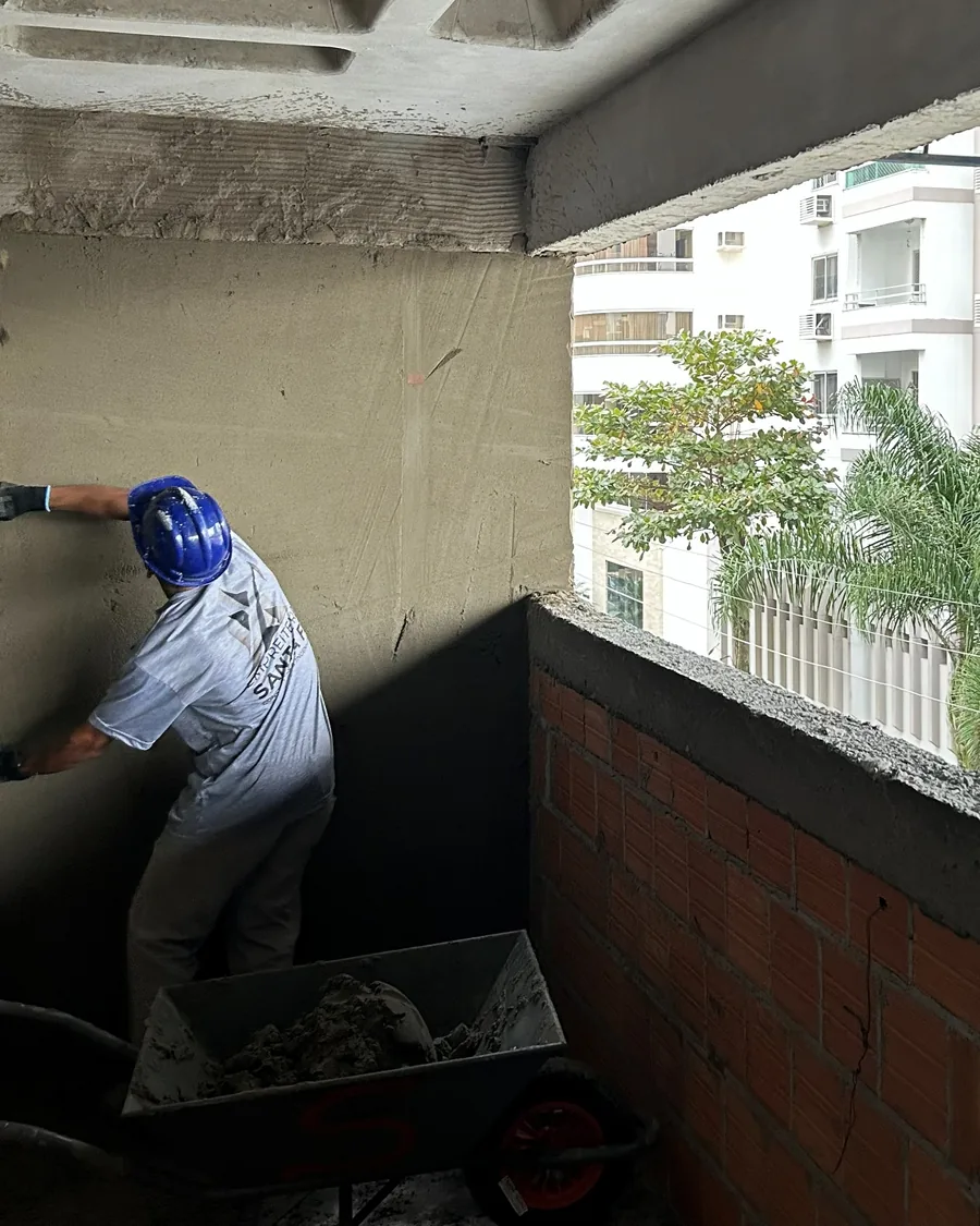 Colaborador aplicando argamassa em parede externa, com masseira ao lado